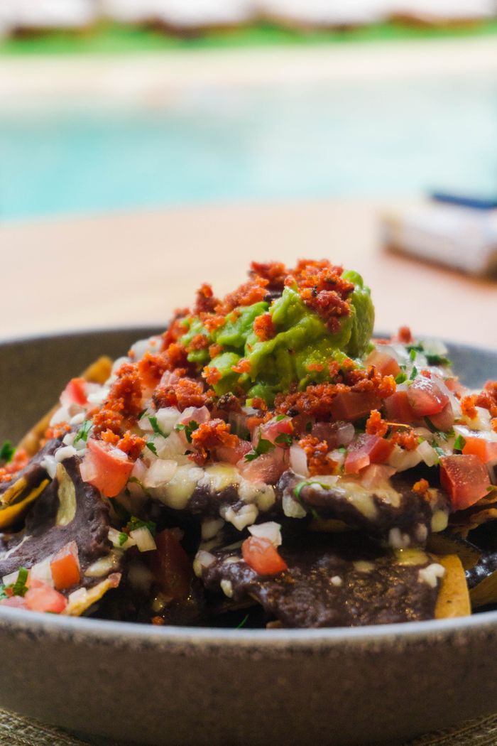 Appetizing Mexican nachos topped with guacamole, salsa, and chorizo to enjoy by the poolside.