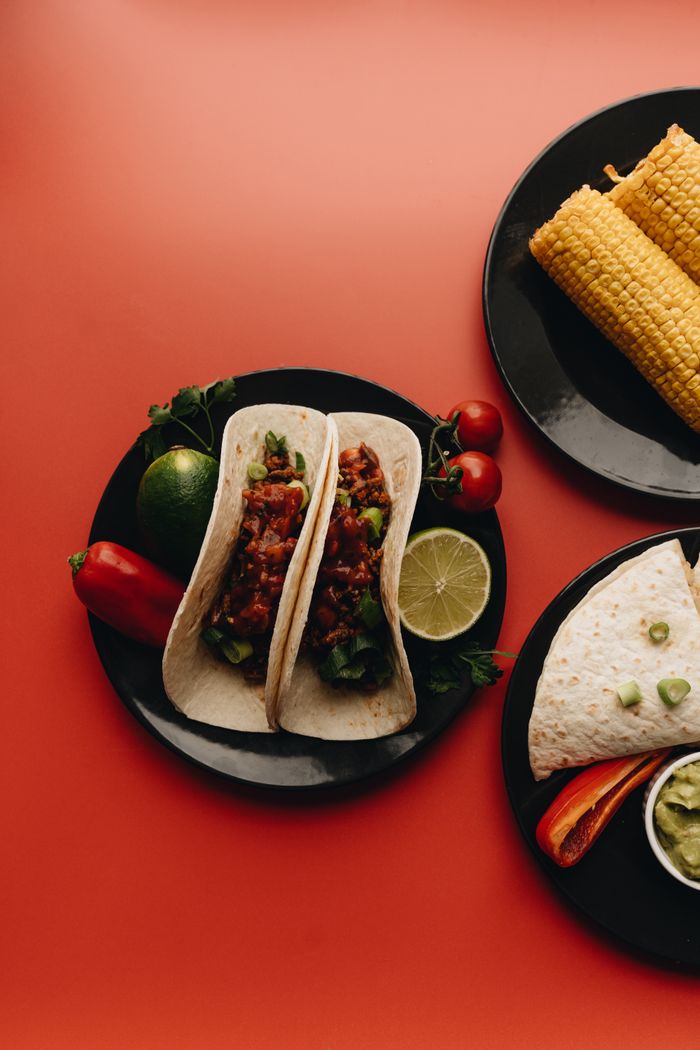 gallery-04 A vibrant food photo showcasing Mexican tacos and fresh vegetables on a red background.